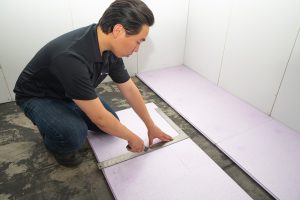 Male in black shirt installing purple DRICORE subfloor into a basement.